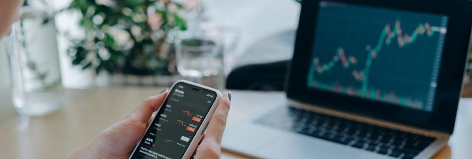 Live trading session with multiple screens: a laptop and smartphone displaying financial charts.