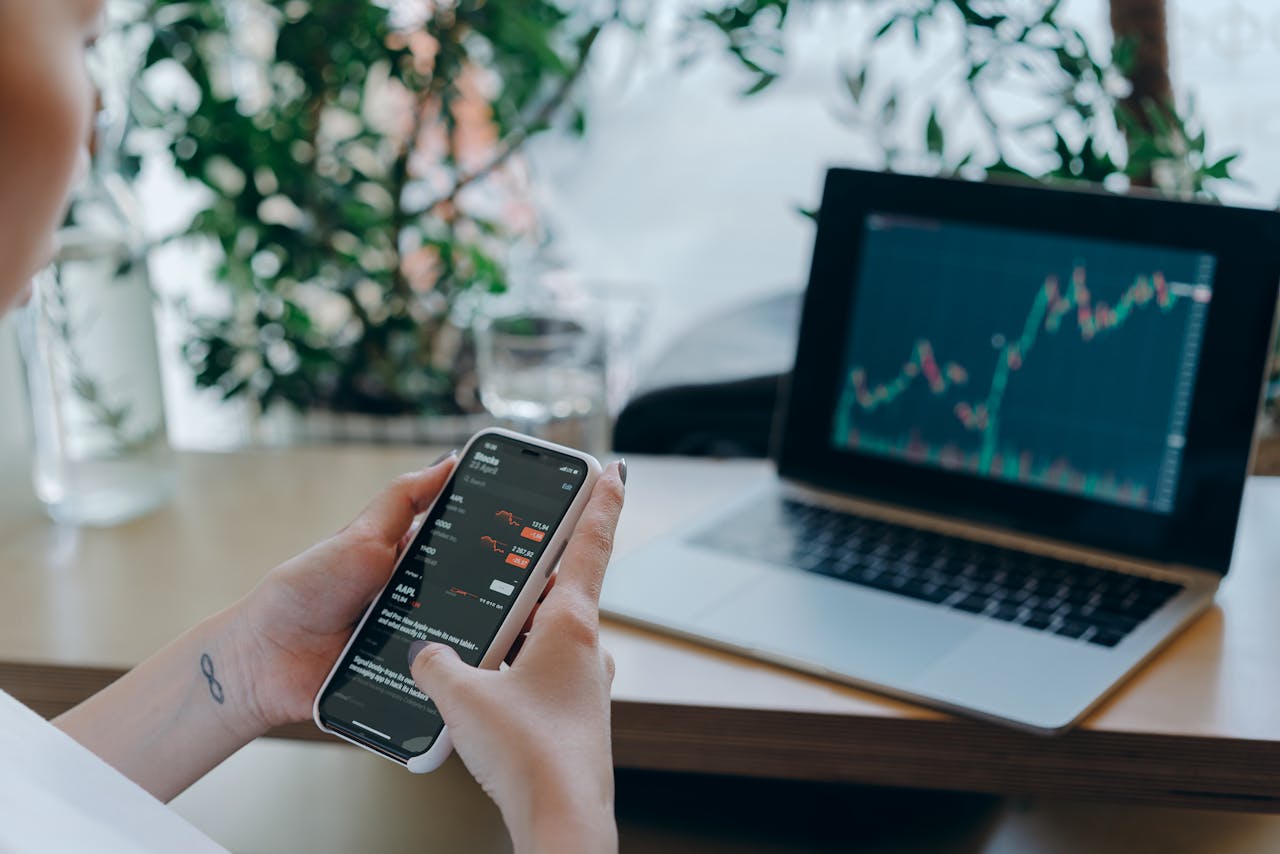 Live trading session with multiple screens: a laptop and smartphone displaying financial charts.